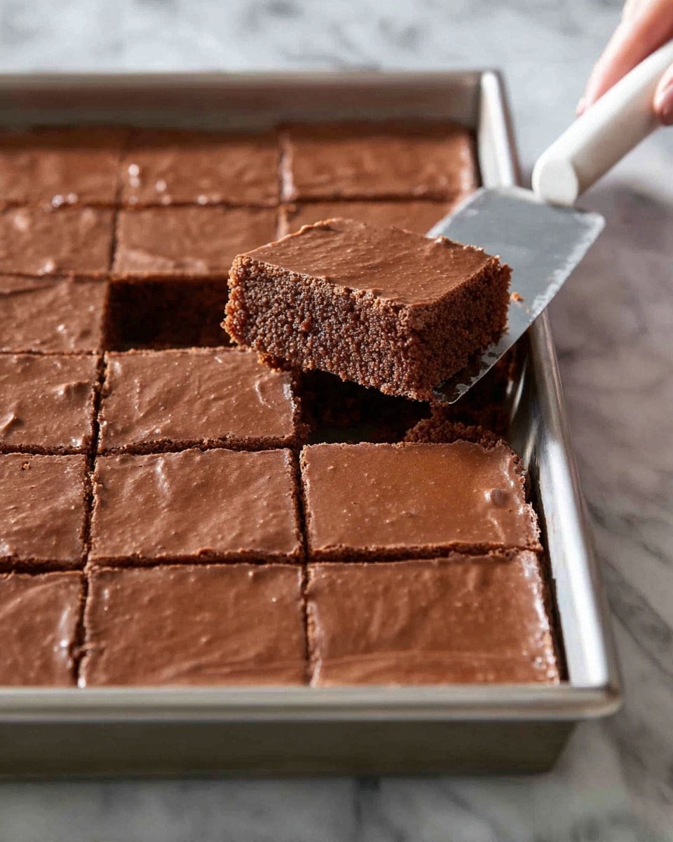 A large rectangular chocolate dessert is shown in a metal baking tray on a white marbled surface. The dessert is cut into even square pieces with smooth, shiny, light brown tops and slightly darker brown, moist and crumbly interiors. There is one piece being lifted from the tray with a metal spatula that has a white handle held by a woman's hand. The texture looks soft and slightly dense with a thin, smooth crust on top. The whole dessert is arranged in a grid of squares ready to serve photo taken with an iphone --ar 4:5 --v 7