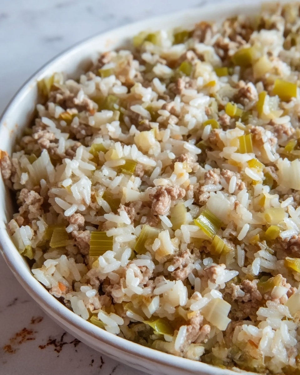 A close-up view of a white bowl filled with a mixture of white rice, small pieces of light brown cooked ground meat, and chopped pale green and white vegetables, all blended together. The texture shows the rice grains separate but moist, with the meat finely crumbled and evenly distributed. The chopped vegetables look soft and cooked, adding some small variation in color. The bowl is placed on a white marbled surface with subtle details visible around its edges. Photo taken with an iphone --ar 4:5 --v 7