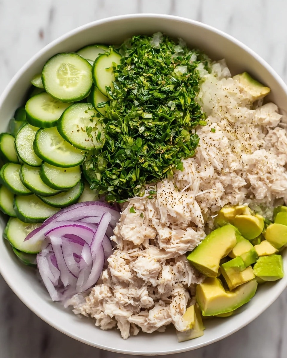 A white bowl filled with four separated layers of food, arranged in sections from left to right: thinly sliced cucumber pieces, finely chopped green herbs piled in the center, pieces of light beige shredded chicken sprinkled lightly with black pepper, thin rings of light purple onion, and diced light green avocado in one corner, all placed on a white marbled surface. Photo taken with an iphone --ar 4:5 --v 7