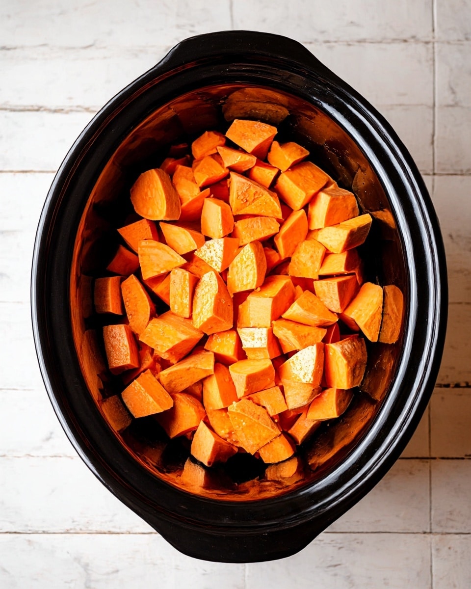 A black slow cooker filled with two layers of chopped sweet potatoes, the pieces showing bright orange color and a slightly shiny texture, evenly spread inside the cooker. The background features a white marbled texture, adding a clean and simple look. photo taken with an iphone --ar 4:5 --v 7