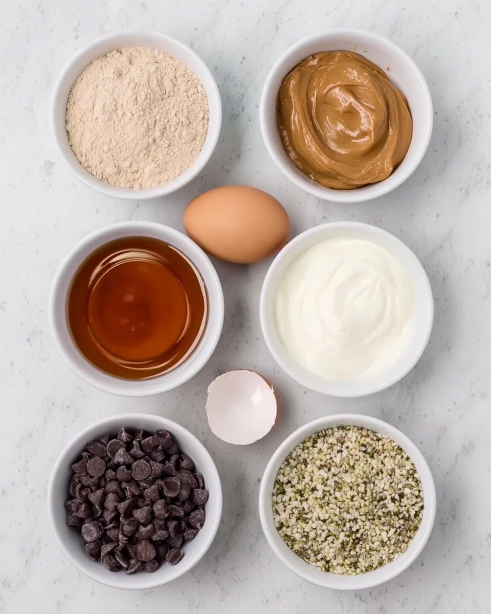 The image shows eight small white bowls arranged in two rows on a white marbled surface. The top row from left to right has a bowl filled with light beige powder, a bowl with smooth brown peanut butter, and a bowl with creamy white yogurt. The bottom row includes a bowl with dark amber maple syrup, a bowl filled with small dark chocolate chips, a bowl with a white cracked eggshell, and a bowl containing light greenish hemp seeds. All bowls are neatly displayed with no spills, showcasing different textures and colors clearly. Photo taken with an iphone --ar 4:5 --v 7