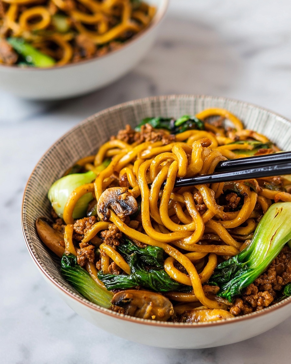 The image shows a bowl filled with thick, glossy yellowish-brown noodles mixed with cooked ground meat pieces and green leafy vegetables. There are visible slices of cooked mushrooms and light green baby bok choy leaves in the bowl. A pair of black chopsticks is picking up some noodles close to the center. The bowl is white with a pattern inside, placed on a white marbled surface. In the background, there is a blurred similar bowl. photo taken with an iphone --ar 4:5 --v 7