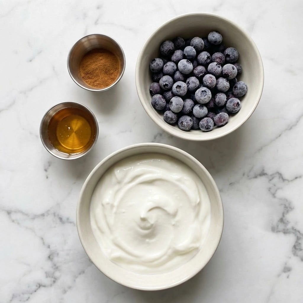 The image shows four small dishes on a white marbled surface. The largest white bowl at the bottom holds a thick layer of smooth, white yogurt with soft peaks. Above to the right, a medium white bowl is filled with a single layer of frozen blueberries, showing a deep purple color with a frosty texture. To the left of the blueberries, a small stainless steel cup contains a fine brown powder, likely cinnamon, in a thin layer. Below it, another stainless steel cup holds a shallow layer of golden honey, shining softly. The setup is clean and simple, emphasizing the natural colors and textures of the ingredients. photo taken with an iphone --ar 4:5 --v 7