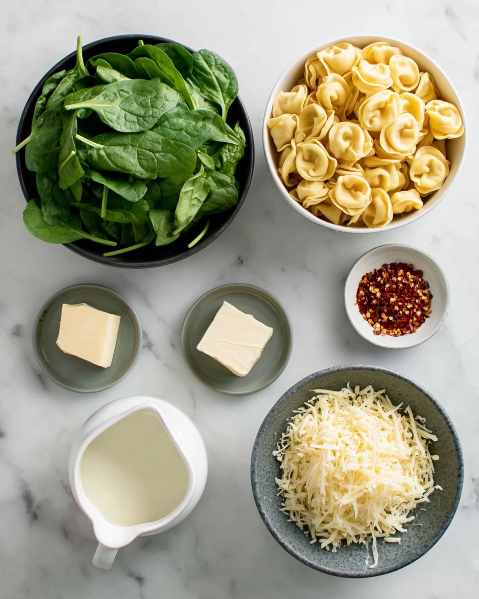 A top view of ingredients for a meal arranged on a white marbled surface: a black bowl full of fresh green spinach leaves on the left, a white bowl filled with yellow tortellini pasta at the top right, a small gray dish with a piece of pale light butter beside it, a larger dark bowl full of pale shredded cheese below the butter, a small gray dish containing red chili flakes just below the center, and a white pitcher with creamy white liquid labeled cream on the bottom left photo taken with an iphone --ar 4:5 --v 7