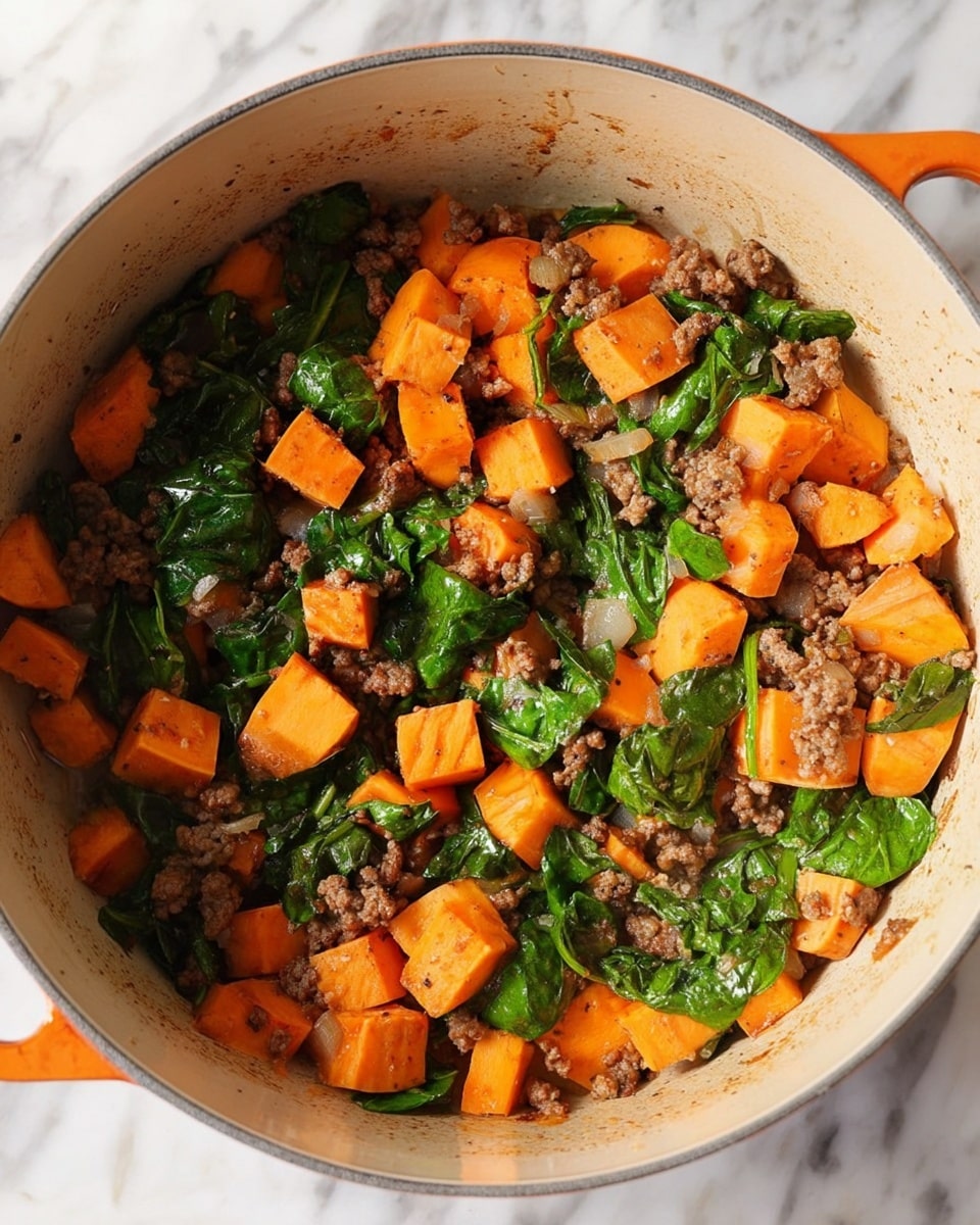 A pot filled with a cooked dish showing three main layers mixed together: bright orange cubes of sweet potato with smooth surfaces, small pieces of brown cooked ground meat, and dark green spinach leaves with soft texture, all cooking evenly inside the beige pot with light marks around the sides. The pot rests on a white marbled surface. photo taken with an iphone --ar 4:5 --v 7