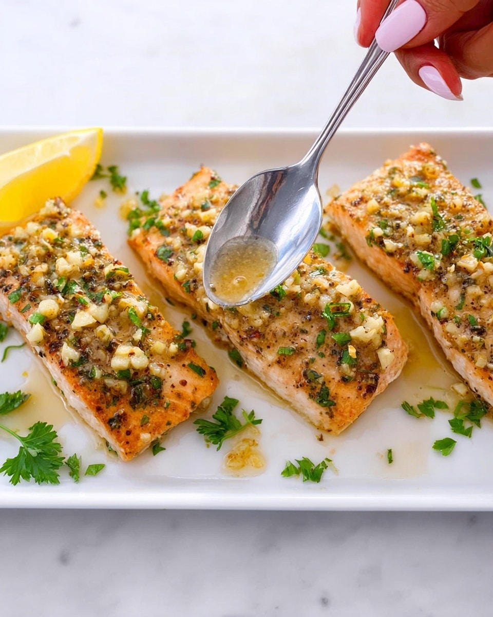 The image shows three pieces of golden-brown cooked fish arranged in a row on a white plate. Each piece is topped with a layer of finely chopped garlic and herbs, giving a textured, slightly moist look on the surface. Small green parsley leaves are scattered around and on top of the fish pieces, adding bright green color. A lemon wedge is placed near the fish at the top of the plate. A woman's hand with light pink nails holds a silver spoon above the middle fish piece, drizzling a shiny garlic and herb sauce over it. The plate sits on a white marbled surface. Photo taken with an iphone --ar 4:5 --v 7