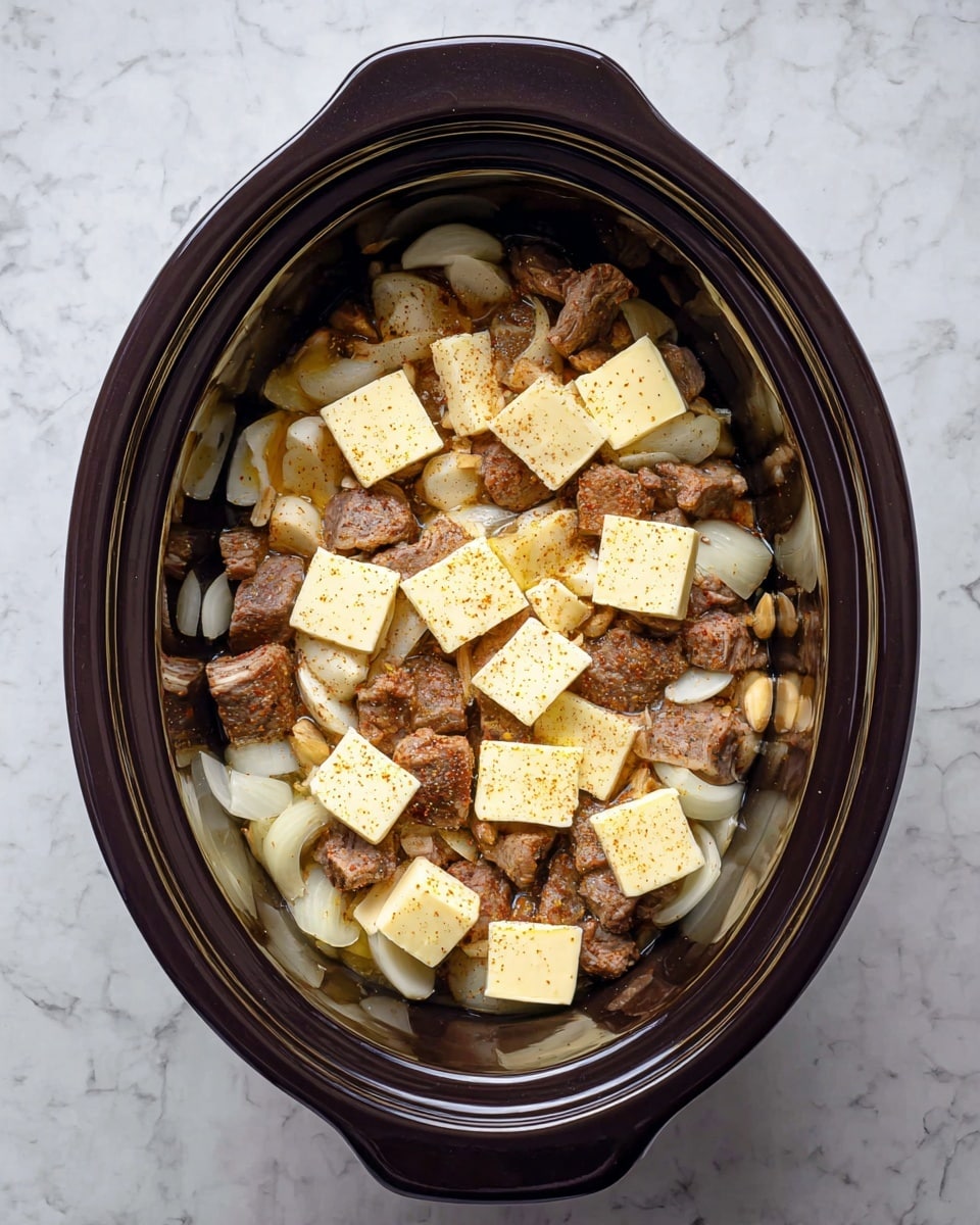 A dark brown oval crockpot holds a layered dish. The bottom layer is light yellow onion slices with a slightly soft texture, scattered with small pieces of pale yellow garlic. On top of that are chunks of brown cooked meat, showing a mix of darker and lighter browned surfaces. On the surface, there are multiple square pats of pale yellow butter spaced evenly across the meat, and a sprinkling of light brown seasoning powder. The crockpot sits on a white marbled textured surface. photo taken with an iphone --ar 4:5 --v 7