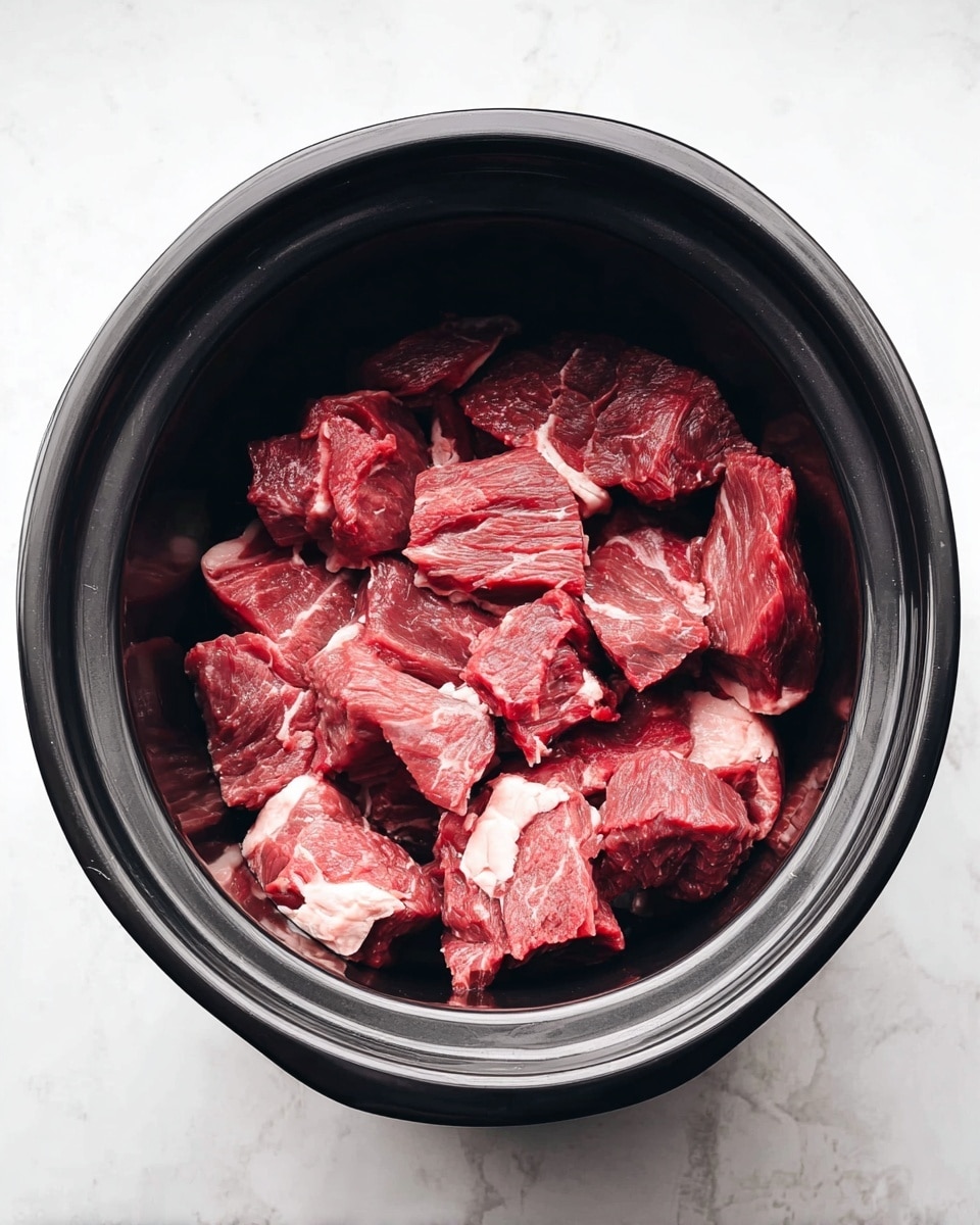 Inside a black slow cooker, there are many pieces of raw red meat with white fat marbling. The meat pieces are piled around three layers deep, showing a mix of smooth and slightly rough textures. The slow cooker sits on a white marbled surface, creating a clean and bright background. The scene is simple and focused on the fresh meat inside the black pot, photo taken with an iphone --ar 4:5 --v 7