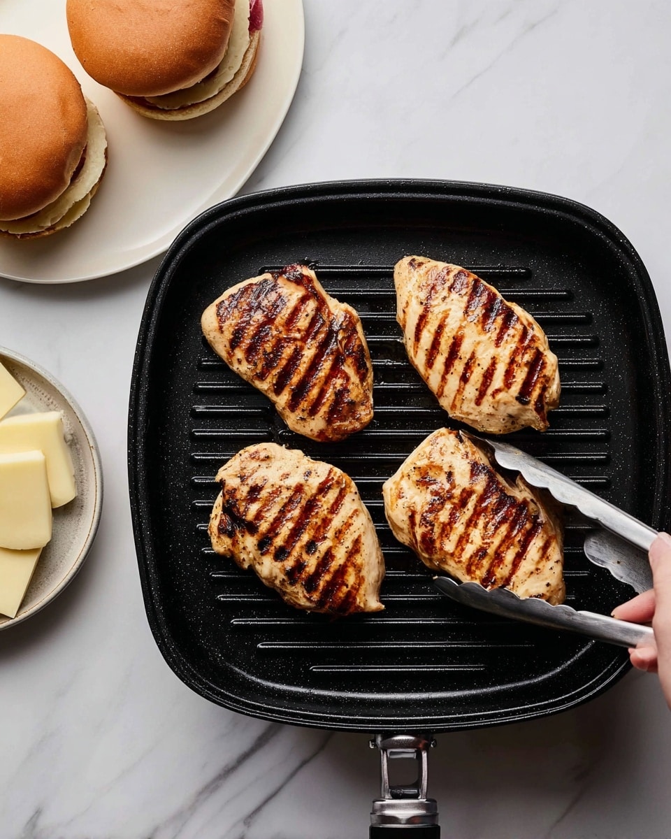 Four grilled chicken pieces with dark grill marks are placed on a black grill pan with slits. The chicken pieces are arranged in a roughly square shape, two on top and two on bottom. A pair of metal tongs held by a woman's hand is lifting the bottom left piece. To the right, there is a white plate with two toasted burger buns showing grill marks, and above it, a smaller white plate holding round pale slices of cheese. All of this is set on a white marbled surface. photo taken with an iphone --ar 4:5 --v 7