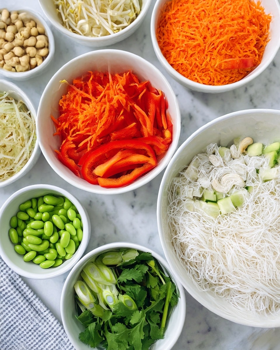 The image shows a top view of several white bowls filled with fresh ingredients arranged neatly on a white marbled surface with a striped cloth nearby. There is one large bowl filled with white noodles at the bottom right. Above it, there is a bowl with bright orange shredded carrots. To the left of the carrots, a bowl holds thinly sliced red bell peppers. Another bowl, located near the top center, contains pale bean sprouts with a crunchy texture. To the right of the bean sprouts, a small bowl is filled with whole cashew nuts. Below the cashews, there is a bowl with sliced green onions showing a mix of dark and pale green layers. On the bottom left, a bowl contains bright green edamame beans, and next to it, near the bottom left center, a smaller bowl holds fresh cilantro leaves. Finally, to the right of the green onions, there is a bowl filled with small cubes of light green cucumber. The overall scene is colorful, fresh, and clean. photo taken with an iphone --ar 4:5 --v 7