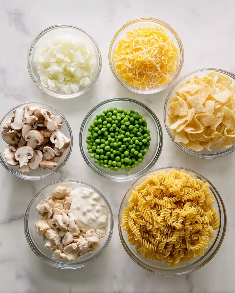 The image shows nine clear glass bowls on a white marbled surface, each filled with different ingredients. The largest bowl contains yellow egg noodles with a curly texture, placed on the right side. Next to it, a medium bowl holds shredded yellow cheddar cheese. Another medium bowl shows small green peas that appear fresh and round. One bowl contains diced white onions with a smooth texture, while another has sliced mushrooms with a brown and beige look. One bowl is filled with creamy white sauce, and another has light beige cooked chicken pieces with a slightly crumbly texture. There is also a bowl holding pale yellow potato chips, and another contains a mix of white and darker bits, likely diced or chopped chicken. All elements are spaced neatly on the white marbled surface photo taken with an iphone --ar 4:5 --v 7