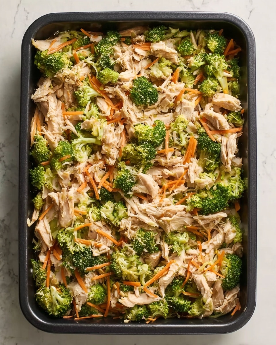 A rectangular black pan filled with a layered dish starting with a base of shredded light-colored chicken pieces evenly spread, mixed with fresh green broccoli florets scattered throughout, and thin, orange carrot sticks placed in between the chicken and broccoli. The textures show tender chicken, crisp broccoli, and soft carrot sticks, all blended together without sauce visible on top. The pan is placed on a white marbled surface. photo taken with an iphone --ar 4:5 --v 7