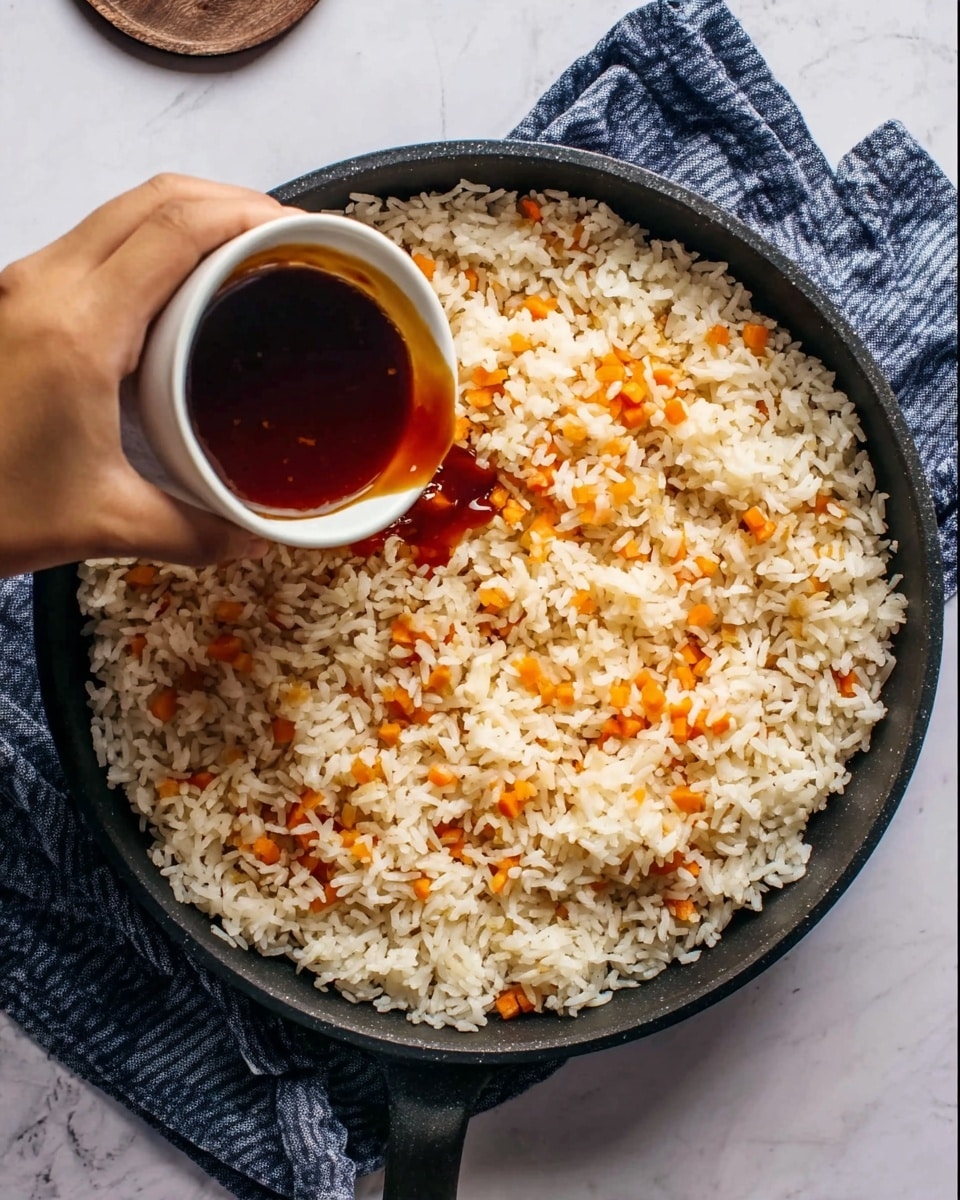 A black pan filled with cooked white rice mixed with small orange carrot pieces forms the base layer. Above this, a white small cup with dark brown sauce is being poured over the rice by a woman's hand, positioned from the top left corner. The pan sits on a white marbled surface with a blue striped cloth partially visible underneath. The rice texture looks soft and fluffy with color contrast between the white rice and orange carrots. photo taken with an iphone --ar 4:5 --v 7