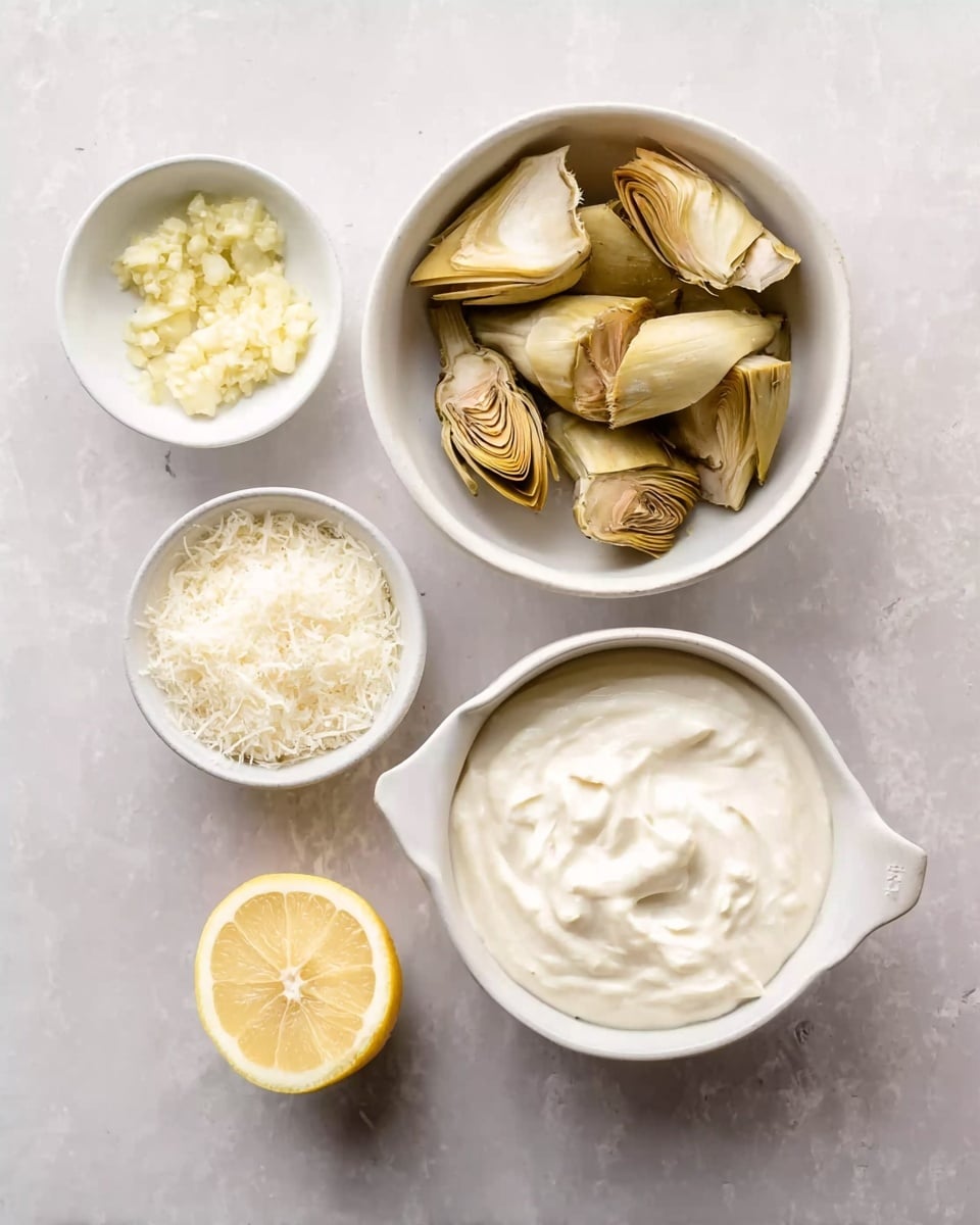 A top view of five bowls arranged on a white marbled surface. The largest bowl on the top left is white, filled with several pieces of artichoke with a light yellow-brown color, showing soft layered leaves. To its right is a white bowl with a small handle, filled with thick white creamy sauce with smooth texture and swirls on the surface. Below the sauce bowl, a small white bowl holds finely grated white cheese. To the left of the cheese bowl, another tiny white bowl contains minced garlic with pale yellow and white bits. In the center bottom, there is a half lemon with bright yellow color and visible segments. Photo taken with an iphone --ar 4:5 --v 7
