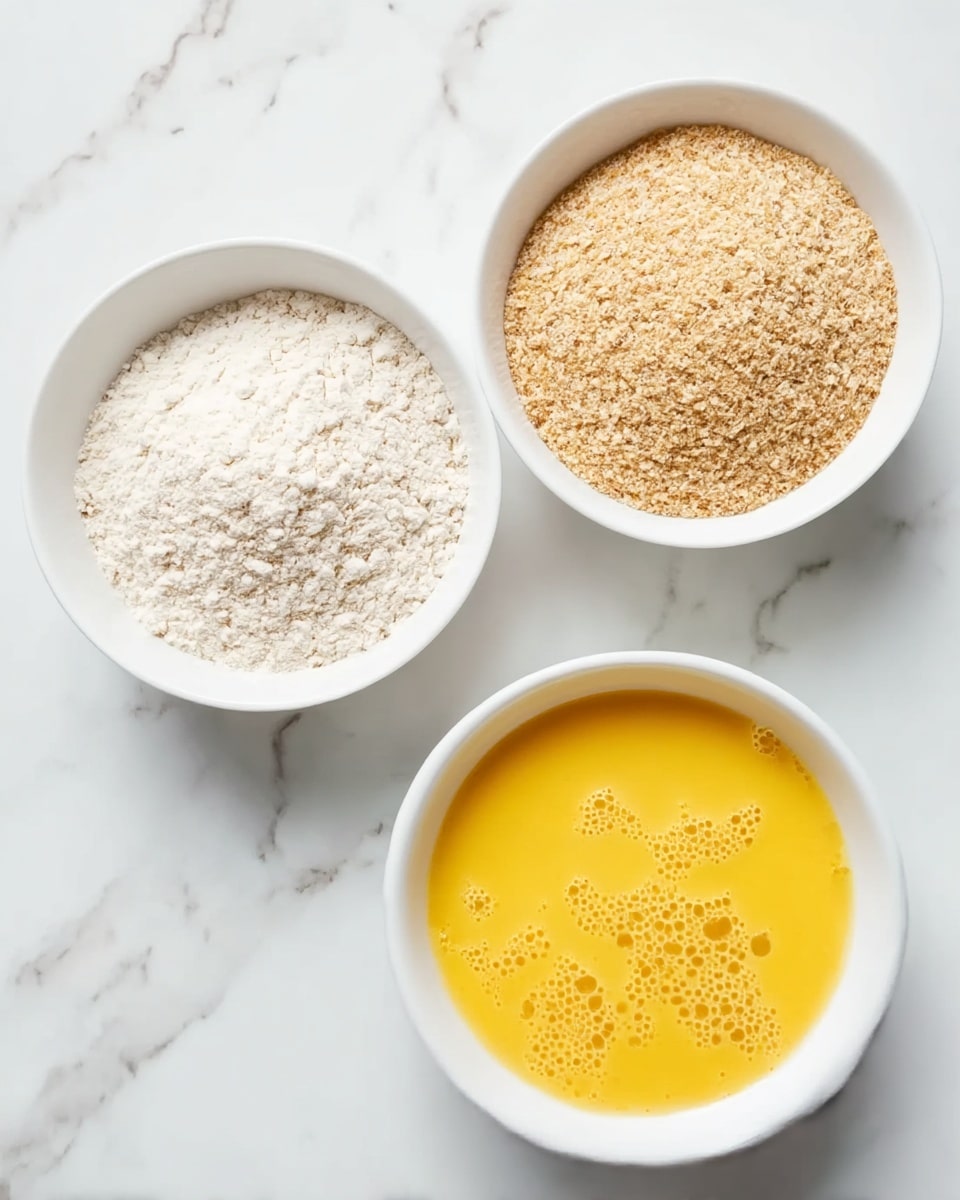 The image shows three white bowls placed on a white marbled surface. The top left bowl holds a fine white powder with a slightly rough texture, likely flour. The top right bowl contains a light brown, coarser powder, which looks like bread crumbs or ground grains. The bottom bowl is filled with a bright yellow liquid that appears smooth with some small bubbles on the surface, resembling beaten eggs. The bowls are arranged in a loose triangle from a top-down view. photo taken with an iphone --ar 4:5 --v 7