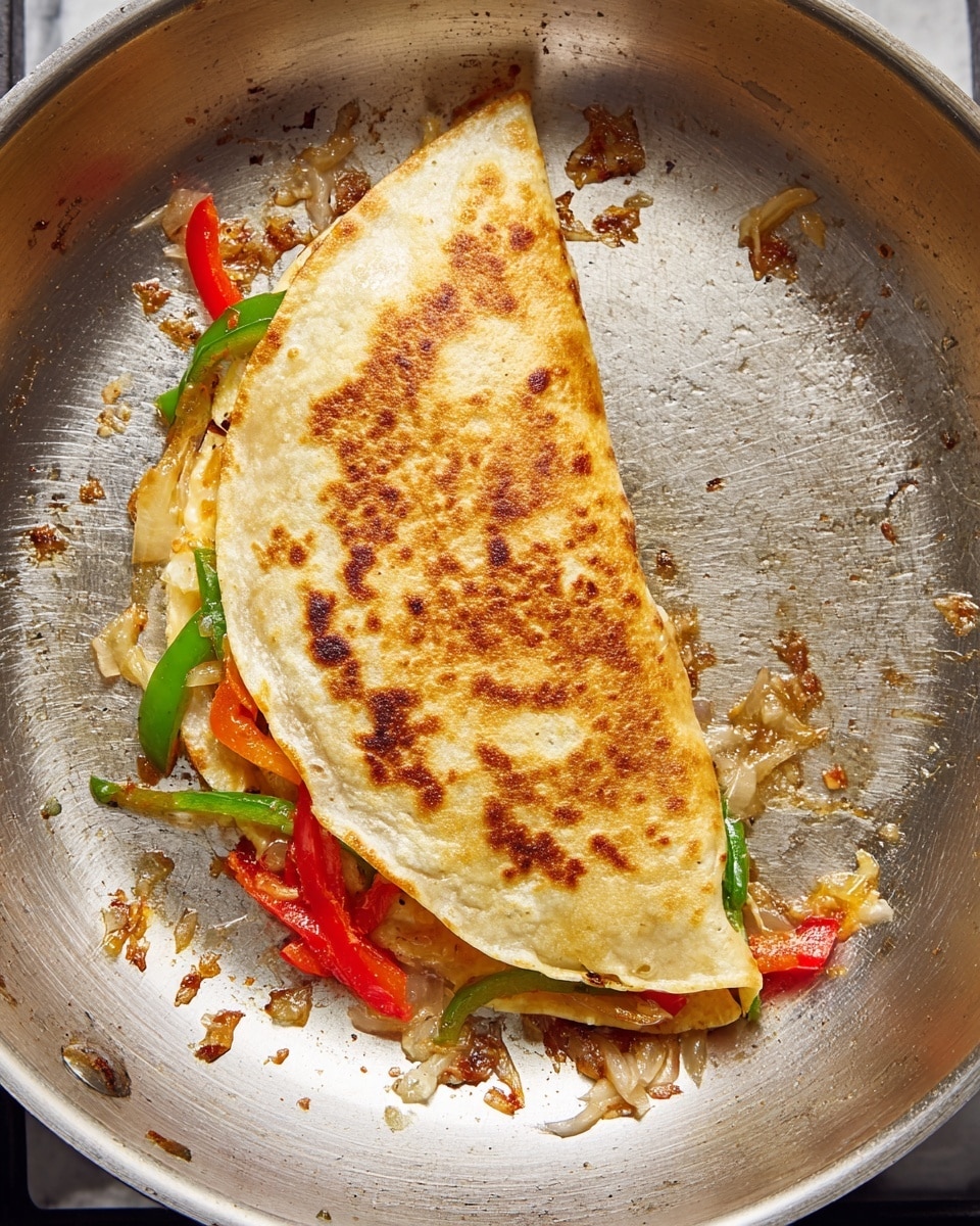 A golden brown folded quesadilla is shown in a silver pan, folded in half with a crispy outer layer that has small darker spots from cooking. Inside, visible layers include melted light yellow cheese, thin slices of red bell pepper, green pepper strips, and some light brown cooked onions. The silver pan has some oil residue and small bits of cooked vegetables scattered around the quesadilla. The photo is taken from above, showing a simple and clear cooking moment. Photo taken with an iphone --ar 4:5 --v 7