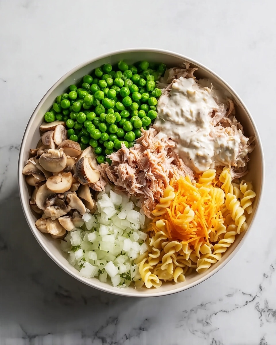 The dish is shown in a white bowl placed on a white marbled surface. Inside the bowl, there are six distinct sections arranged in a circular pattern without mixing, showcasing different ingredients. Starting from the top left and moving clockwise, there are bright green peas with a slightly matte texture, smooth pale brown sliced mushrooms glistening lightly, thick white creamy sauce with specks of herbs, a heap of finely shredded orange cheese, tender light pink shredded tuna, small white chopped onions with a slight shine, and in the center, curly pasta pieces with a pale yellow color and soft texture. The photo taken with an iphone --ar 4:5 --v 7