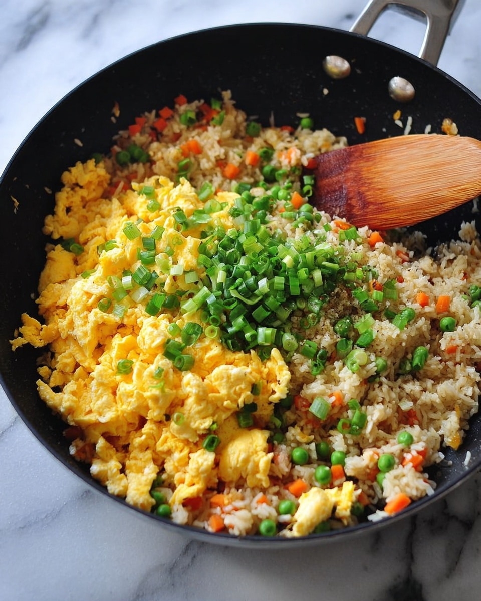 A black pan filled with a layer of cooked rice mixed with small orange carrot pieces and green peas, topped with a layer of bright yellow scrambled eggs, and sprinkled with chopped green onions, with a wooden spatula resting inside the pan, all placed on a white marbled surface photo taken with an iphone --ar 4:5 --v 7