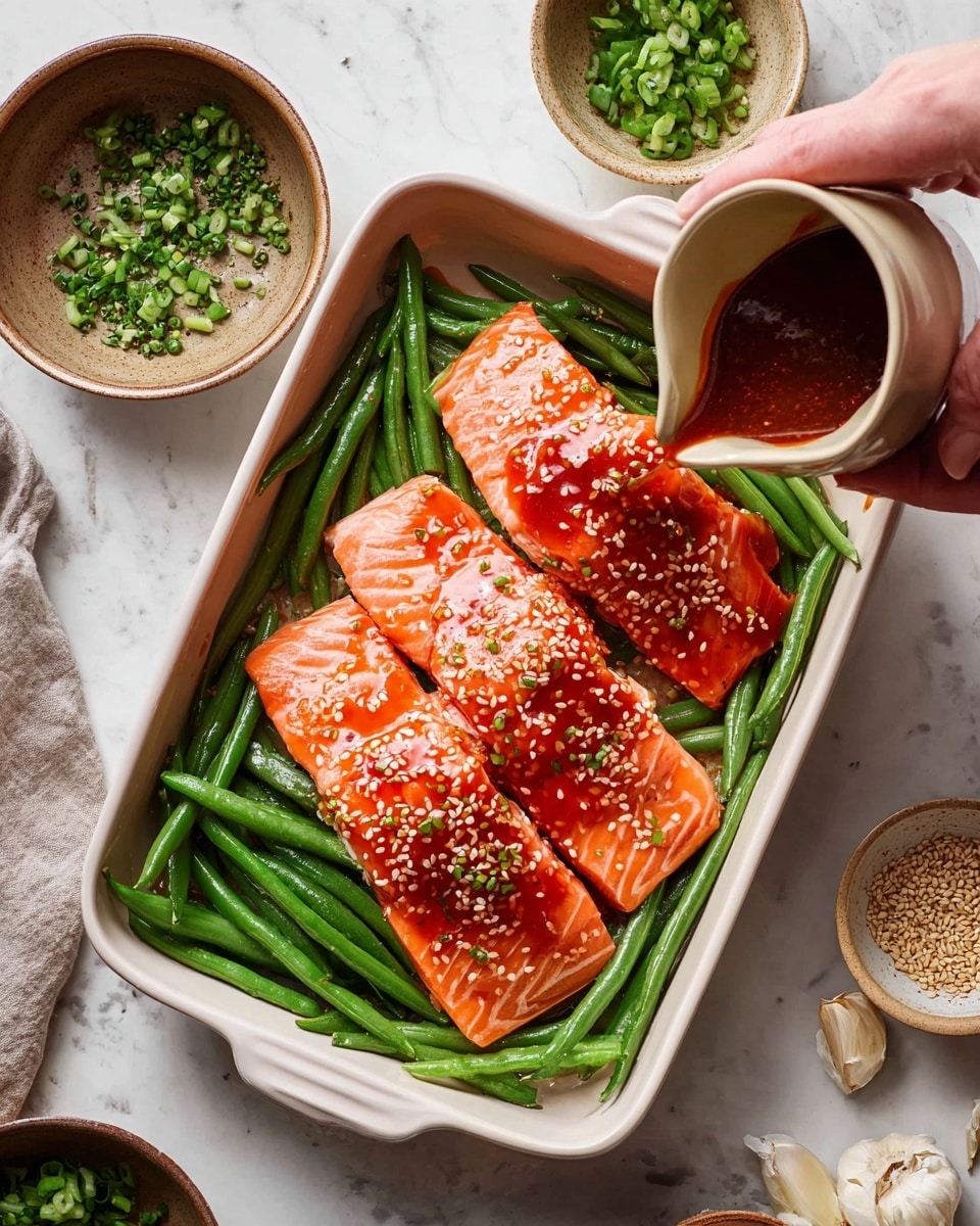 In a white baking dish, there are three thick pieces of fresh, orange-pink salmon placed over a bed of bright green beans. The top of the salmon has a shiny, red sauce with sesame seeds sprinkled on it. A woman's hand is pouring more of this sauce from a small beige pitcher onto the green beans and salmon. Around the dish, a white marbled surface shows some bowls with green chopped herbs, raw green beans, garlic cloves, and sesame seeds. The overall scene is bright with natural lighting, focusing on the rich colors and textures of the ingredients photo taken with an iphone --ar 4:5 --v 7