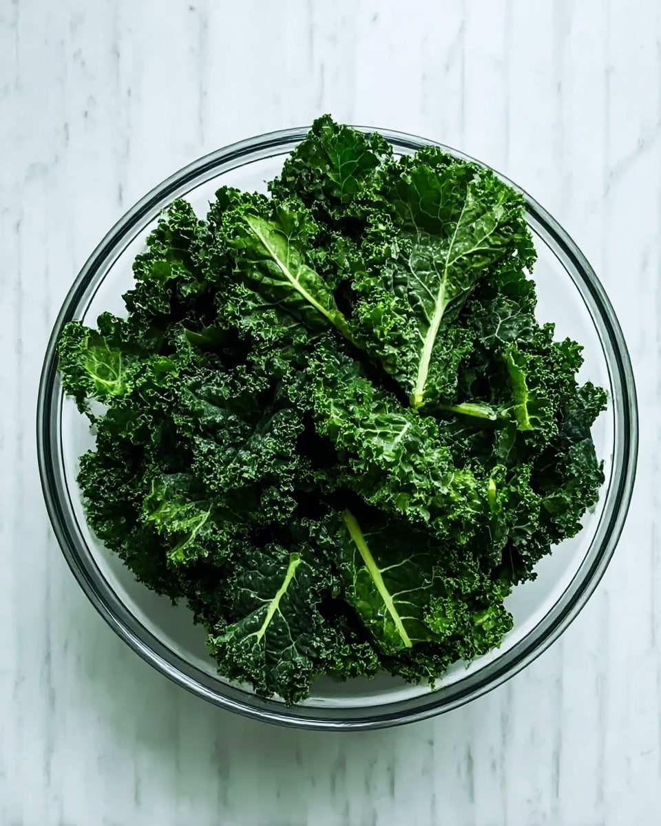 A clear glass bowl filled with many fresh, dark green kale leaves that have a curly and rough texture, showing layers of vibrant greens with some lighter veins. The bowl is placed on a white marbled surface that adds brightness and contrast to the green leaves. The light shines evenly over the kale, making the colors look fresh and lively. photo taken with an iphone --ar 4:5 --v 7