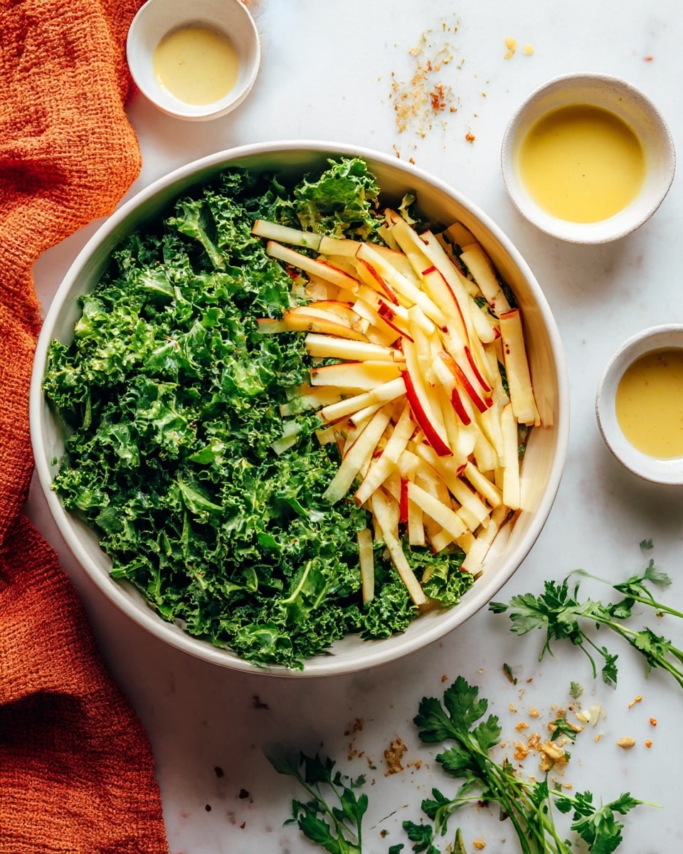 A large white bowl holds a fresh salad with two main layers: on the left side, there is a thick layer of curly kale leaves in bright green, and on the right side, there is a pile of thin, pale yellow apple sticks with red edges. Around the bowl on a white marbled surface, there are small white bowls with light yellow dressing and a light brown creamy sauce, along with scattered bits of herbs and a textured orange cloth. A few sprigs of fresh green herbs rest near the bowl. The photo taken with an iphone --ar 4:5 --v 7