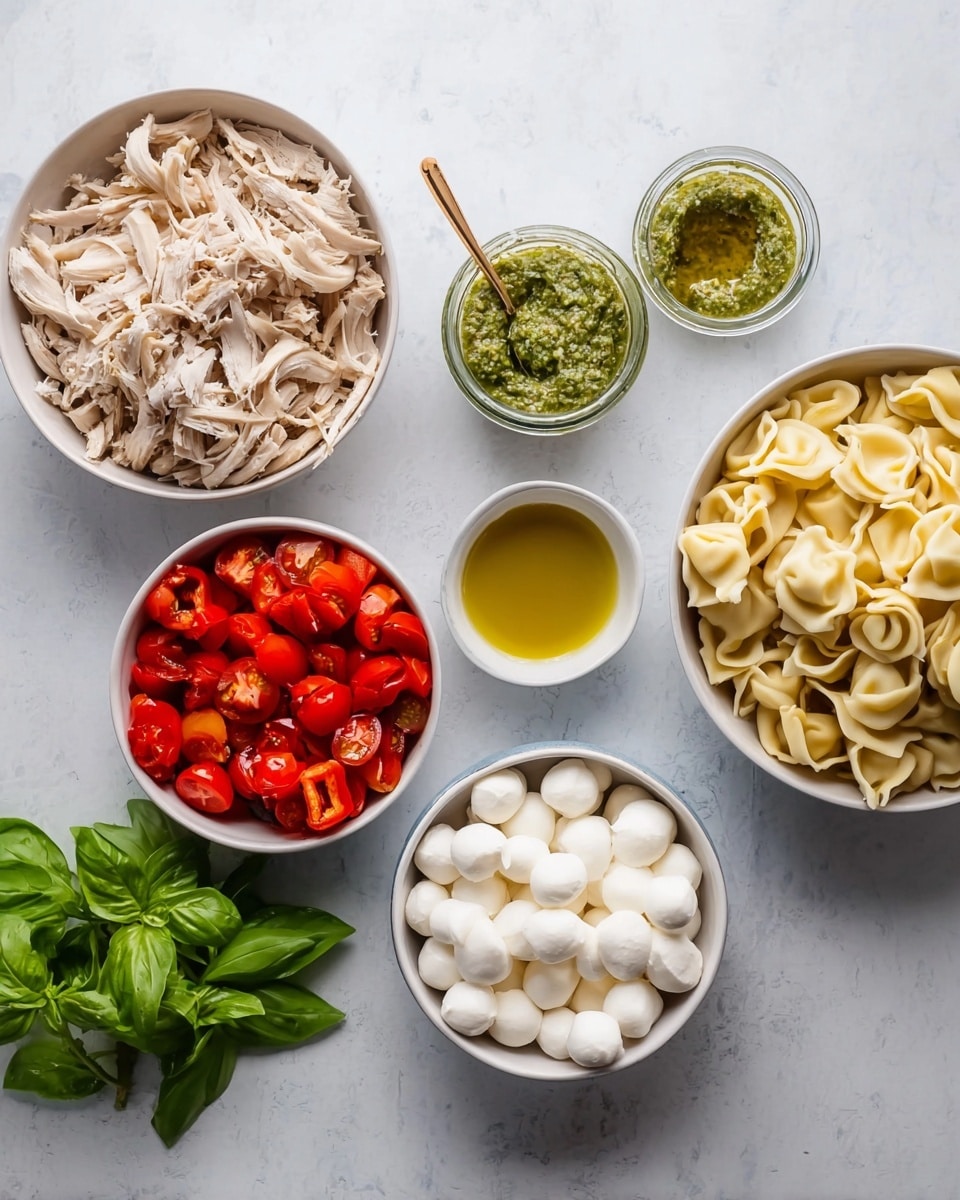There are seven bowls and a small bunch of fresh basil on a white marbled surface. On the left, a large white bowl holds shredded light brown chicken. Next to it, a smaller white bowl has bright red roasted peppers with shiny surfaces. Below, a white bowl contains halved cherry tomatoes showing their red flesh and green seeds inside. In the center, a tiny white bowl is filled with yellow-green olive oil. To its right, another white bowl holds many small white mozzarella balls, smooth and round. Above it, a small glass jar with light green pesto sauce and a gold-colored spoon sits. On the far right, a large white bowl contains pale yellow cooked tortellini with a soft texture. A bunch of fresh green basil leaves with a smooth texture lays near the olive oil bowl. Photo taken with an iphone --ar 4:5 --v 7