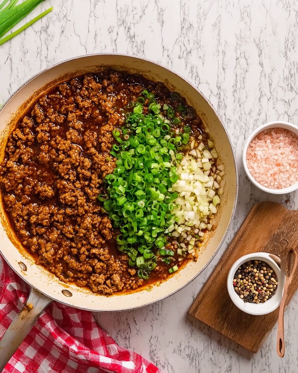 A white frying pan filled with a cooked ground meat mixture in a dark brown sauce takes up most of the image. The pan’s contents are divided into two main parts: on one side is finely chopped white garlic, and on the other side is the rich brown meat sauce topped with a small pile of chopped bright green scallions in the center. The pan sits on a white marbled surface with a red and white checkered cloth partially visible on the left and some green onions nearby. To the right, there is a small white bowl of pink salt and a white container of mixed peppercorns, both placed on a small wooden cutting board. Photo taken with an iphone --ar 4:5 --v 7