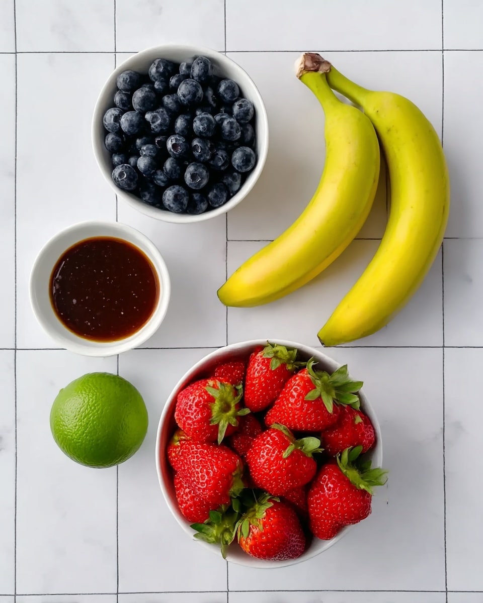 The image shows a neat arrangement of fresh fruit and a small bowl of sauce on a white marbled surface with a grid pattern. At the bottom center, there is a white bowl filled with bright red strawberries, their green leaves still attached, creating a lively contrast. Above the strawberries, slightly right, are two yellow bananas placed side by side with smooth skins. At the top center, there is a white bowl filled with dark blue blueberries, densely packed. To the left center, a whole green lime with a textured skin sits beside a small white bowl filled with a dark brown, glossy sauce. The overall scene is clean and fresh, brightly lit, and balanced in color and layout. Photo taken with an iphone --ar 4:5 --v 7