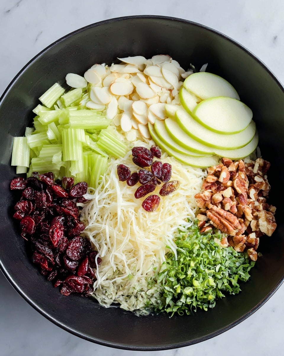 A black bowl filled with six different layers of ingredients neatly arranged in sections: light green celery pieces on the top left, white almond slices above center, thin slices of green apple on the top right, small dark red dried cranberries on the bottom left, shredded white vegetable strands at the bottom center, chopped green herbs on the bottom right, and a pile of chopped brown nuts in the middle. The bowl sits on a white marbled surface. photo taken with an iphone --ar 4:5 --v 7