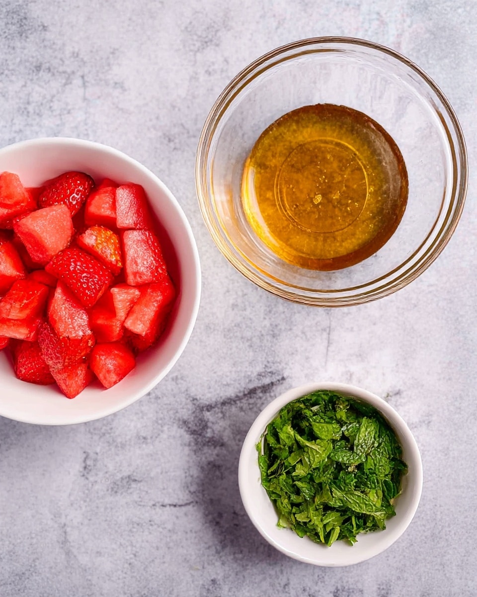 The image shows three bowls placed on a white marbled surface. On the left, there is a white round bowl filled with bright red chopped strawberries and watermelon pieces. In the middle, a clear glass bowl contains a layer of golden honey or syrup at the bottom. To the right, another white bowl holds a small amount of green chopped mint leaves with a fresh texture. photo taken with an iphone --ar 4:5 --v 7
