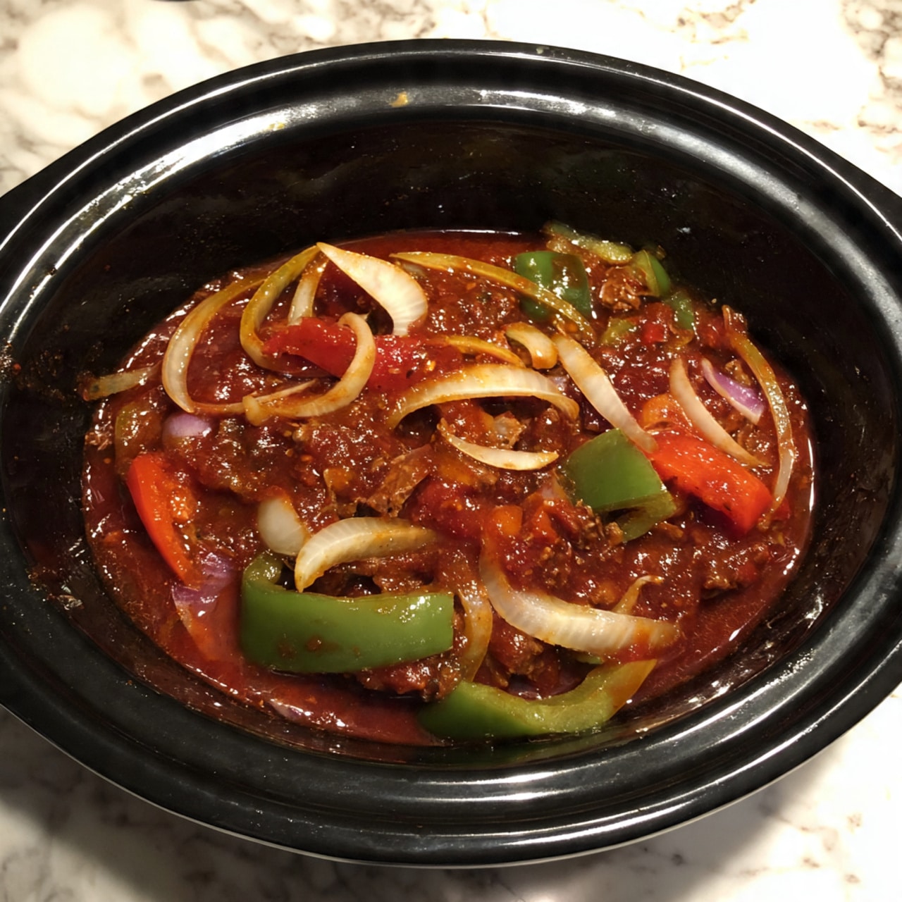 A black slow cooker filled with several layers: the bottom layer is dark brown meat, topped with sliced onions in light purple and green bell peppers. All is covered with a thick, rich red sauce, mixing with the vegetables and meat. The cooker is placed on a white marbled surface. photo taken with an iphone --ar 4:5 --v 7