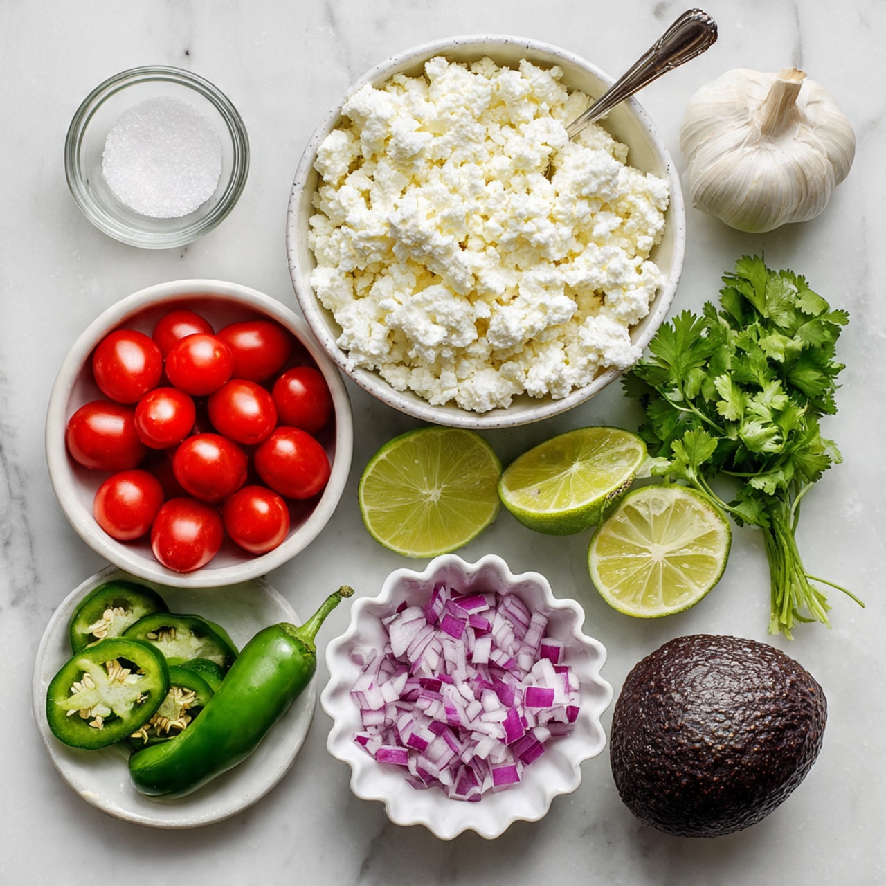 The image shows ingredients arranged on a white marbled surface: a white bowl filled with chunky white cottage cheese with a small metal spoon inside is centered at the top, below it on the left is a small white bowl filled with bright red quartered cherry tomatoes, next to it on the bottom left is a fresh green jalapeño pepper sliced open showing its white seeds, in the middle are two halves of a bright green lime placed side by side, on the right middle a small white scalloped bowl contains finely chopped purple onion, and to the right of it is a whole dark brown avocado with rough skin. Above the onion and avocado, there are two peeled cloves of garlic and a small bunch of fresh green cilantro leaves, and in the top left corner, there is a tiny clear glass bowl filled with coarse white salt. Photo taken with an iphone --ar 4:5 --v 7