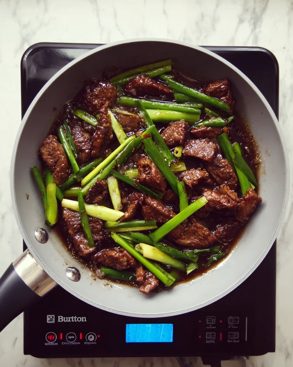 A top view of a light grey frying pan filled with dark brown cooked meat strips mixed with bright green spring onions in a glossy dark sauce. The pan is placed on a black induction stove with buttons and a blue digital screen. The background is a white marbled surface. photo taken with an iphone --ar 4:5 --v 7