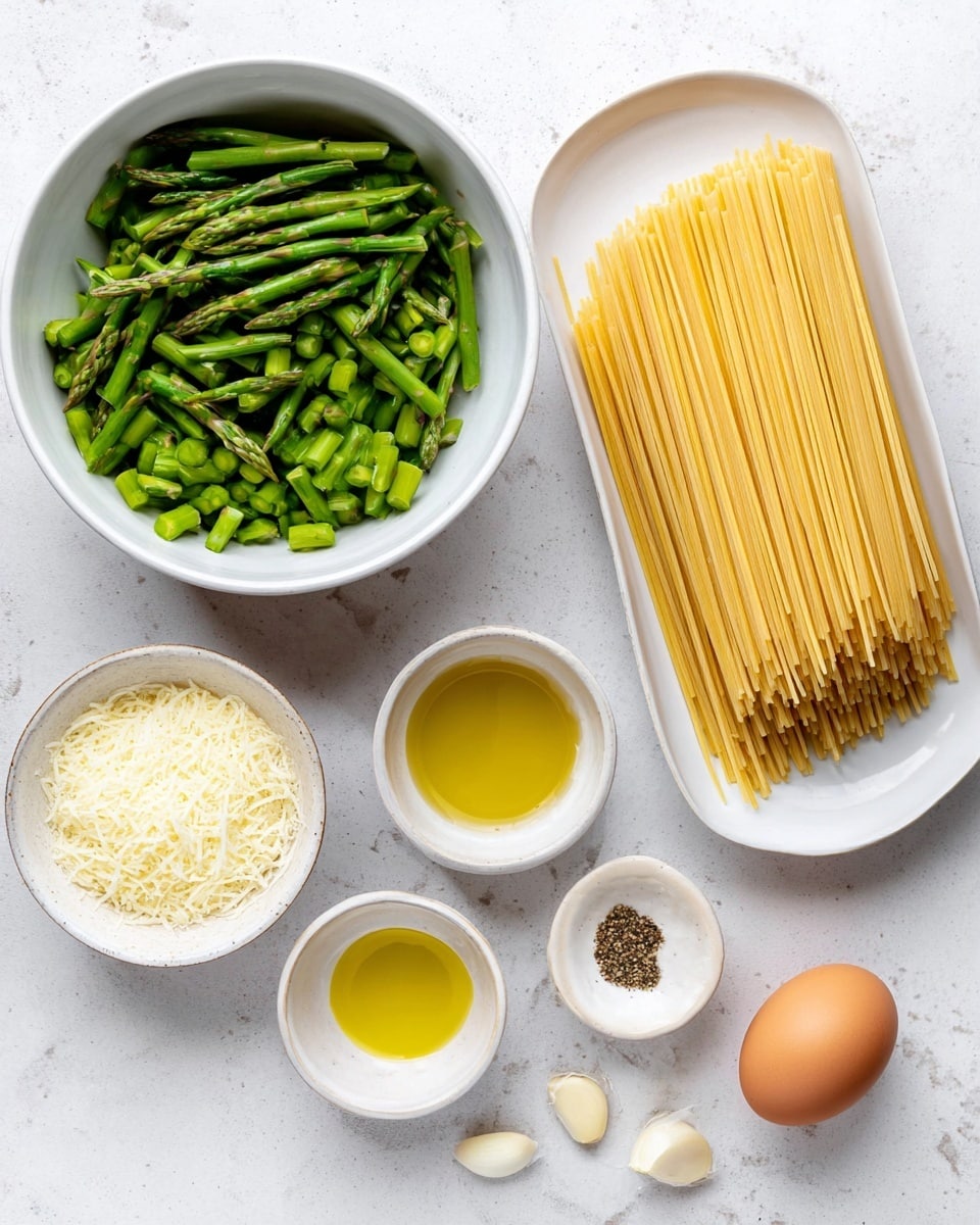 The image shows a white bowl filled with chopped bright green asparagus pieces on the left side. To the right, there is a white oval plate with a neat stack of uncooked pale yellow spaghetti noodles. Above the plate, two small white bowls hold golden olive oil and a mix of black pepper and salt. Below the asparagus bowl is a small white bowl filled with finely grated light yellow cheese. In the lower right corner, there is one brown egg and a small white dish with several peeled garlic cloves. All items are placed on a clean white marbled surface. Photo taken with an iphone --ar 4:5 --v 7